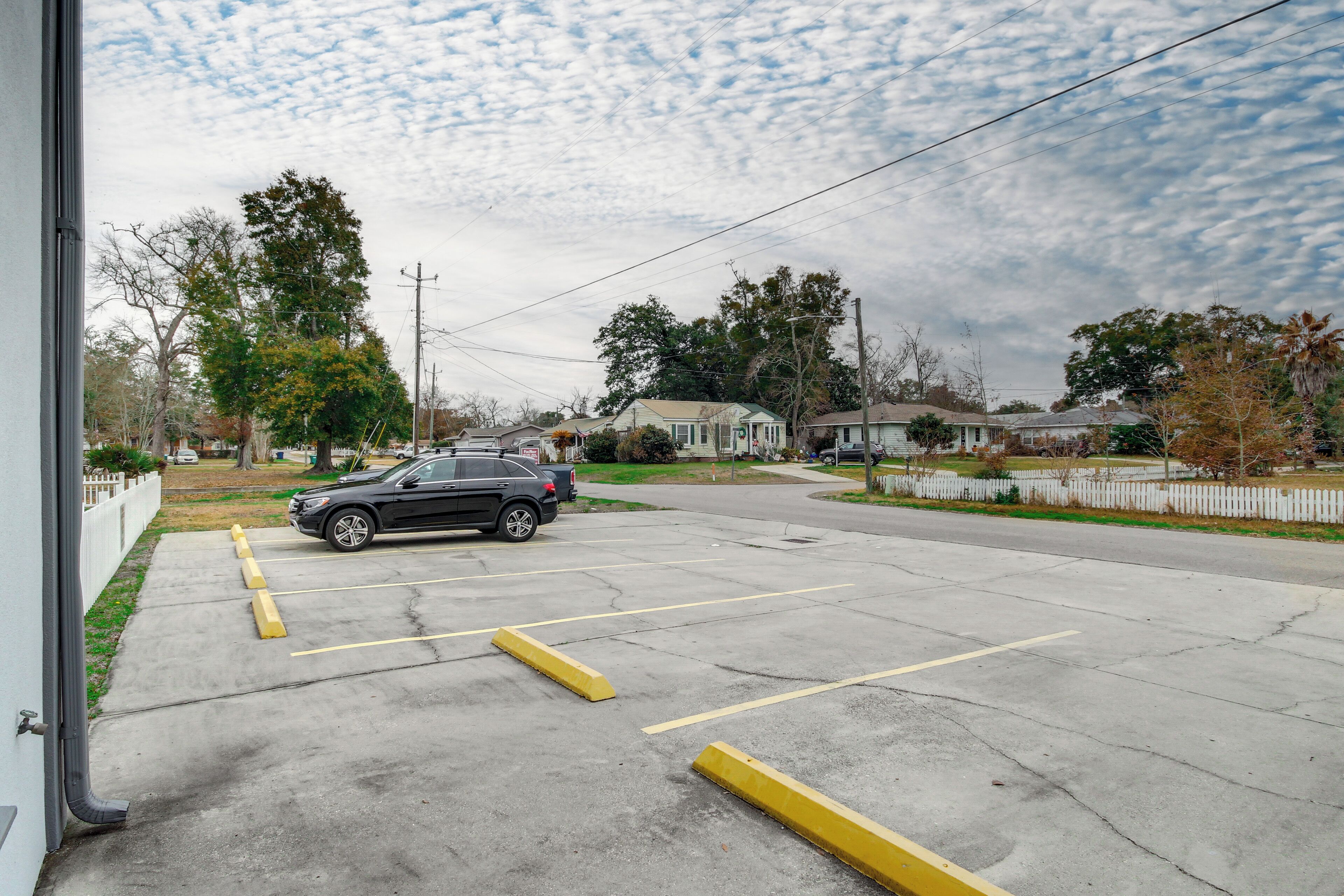 A parking lot with a car parked in the foreground, surrounded by yellow curbs and a white fence.