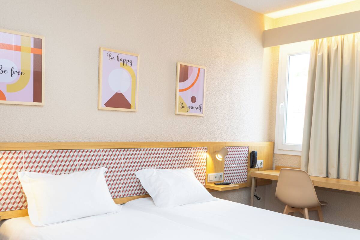 Une chambre d’hôtel avec un lit, un bureau doté d’une lampe et trois affiches inspirantes accrochées au mur.