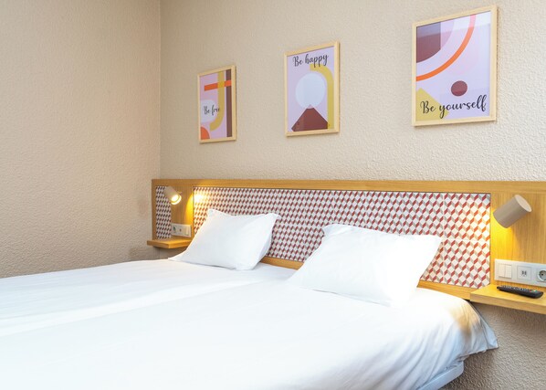 A hotel room with a bed, two bedside tables, a nightstand, and three motivational posters on the wall.