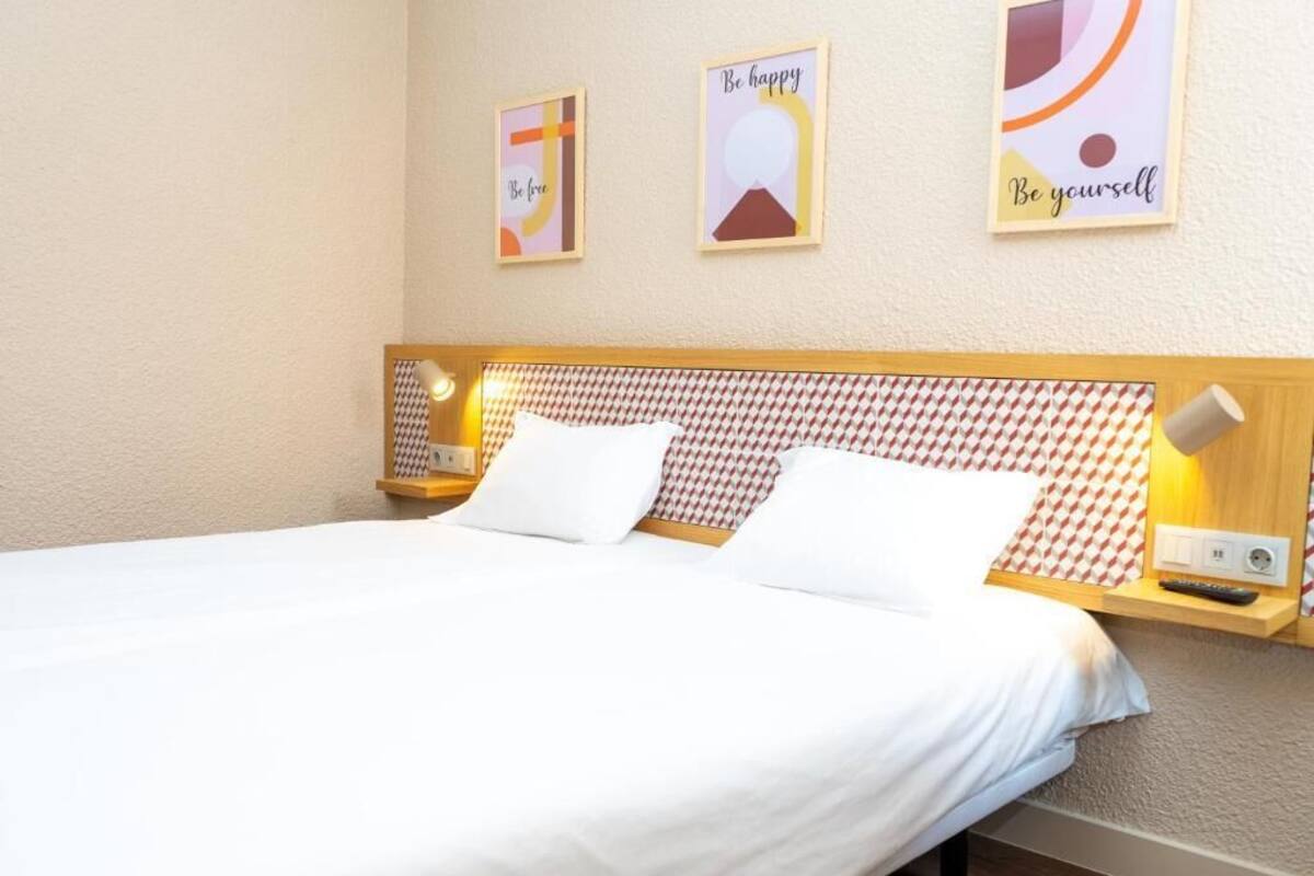 Un lit bien fait, avec du linge de lit blanc, une tête de lit à motifs, des lampes de chevet et des œuvres d’art murales inspirantes.