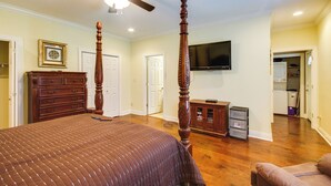 A bedroom with a large bed, a wooden dresser, a ceiling fan, a television, and a hallway leading to a bathroom. - Homey Greenwood Getaway w/ Patio & Backyard (Greenwood)