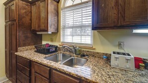 A kitchen with wooden cabinets, a granite countertop, a double sink, a window with blinds, and a toaster. - Homey Greenwood Getaway w/ Patio & Backyard (Greenwood)
