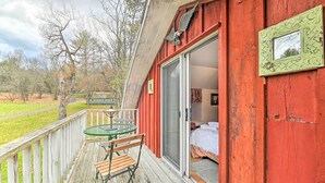 A wooden deck with a table and chairs, a sliding glass door leading to a room with a bed, and a red exterior wall. - Old Time Catskill Mtn Retreat, Handcrafted Cabin! (East Durham)