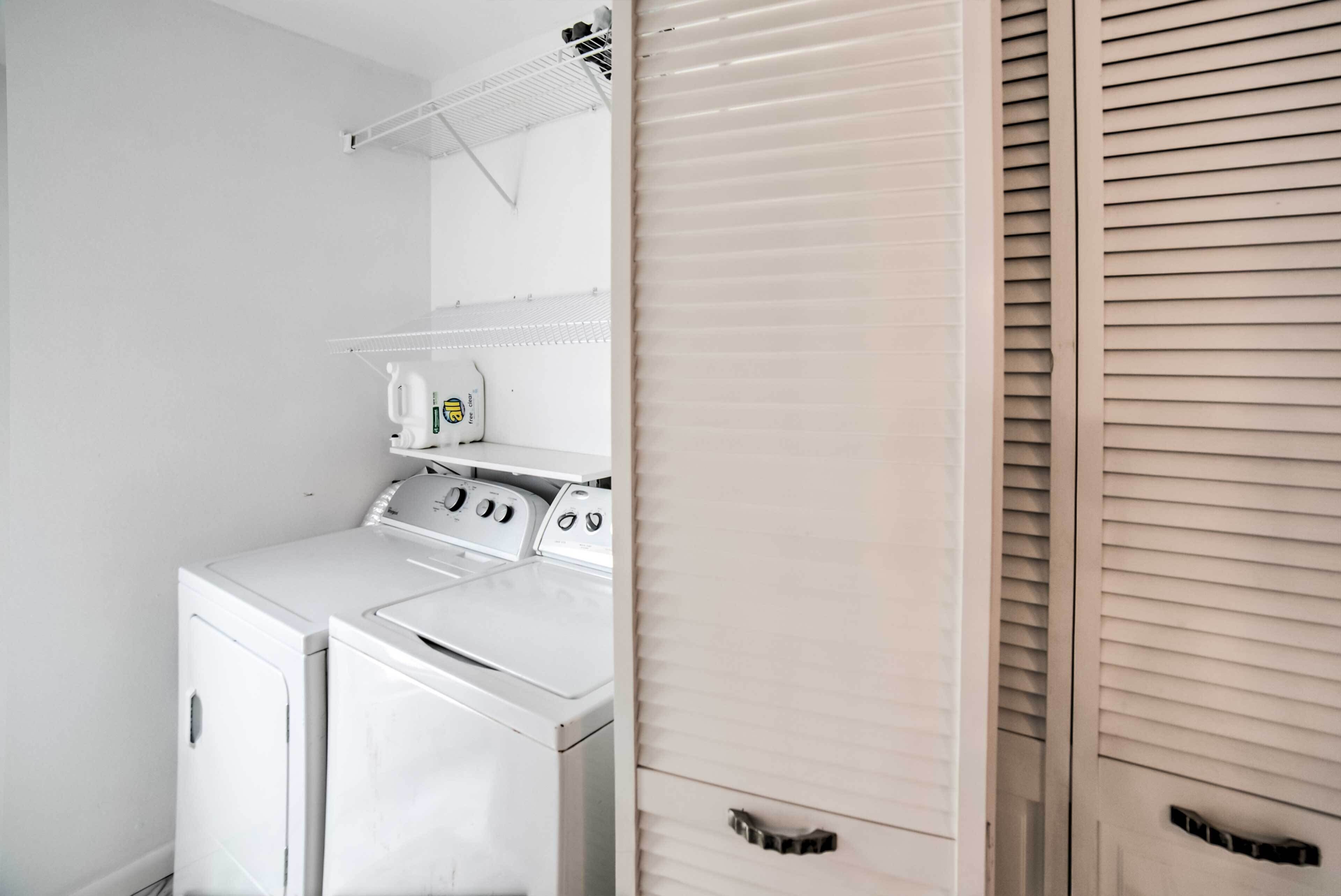 Un espace buanderie comprenant un lave-linge et un sèche-linge, une étagère avec de la lessive et une porte en bois avec une poignée.