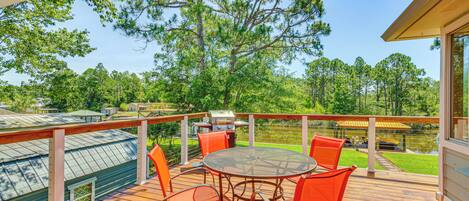 A wooden deck with a round table and orange chairs, overlooking a lake and trees.