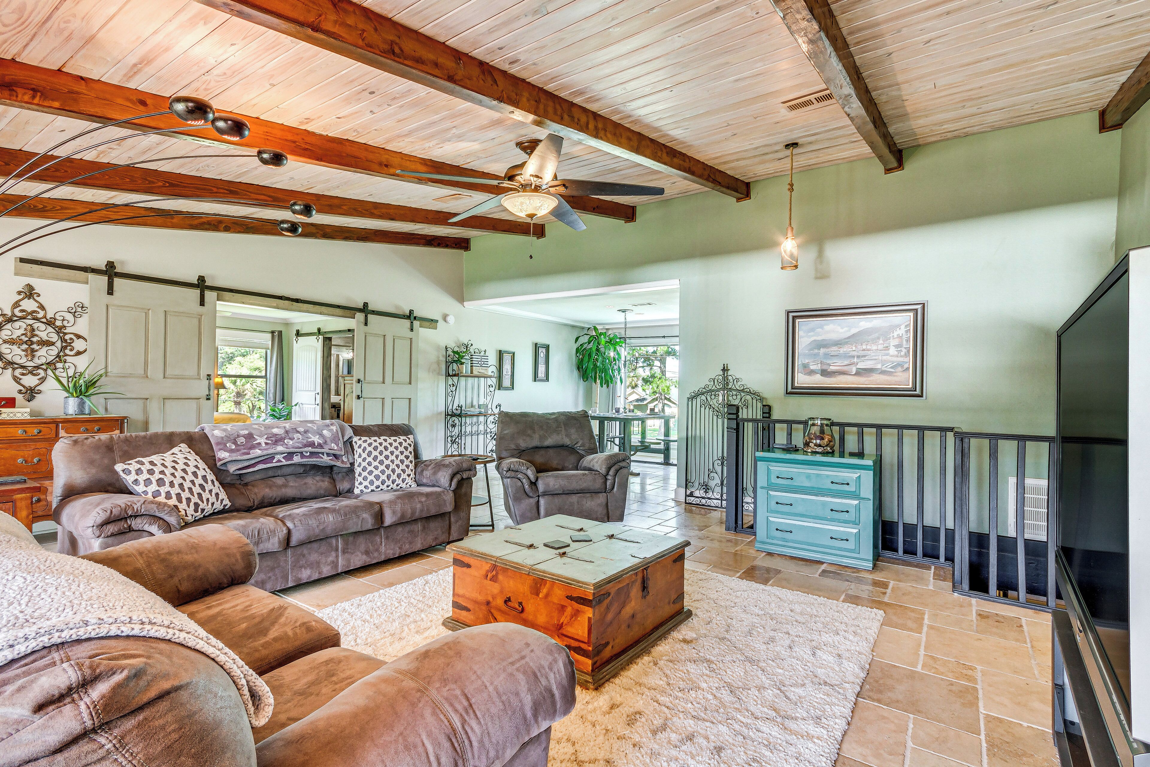 Ein geräumiges Wohnzimmer mit Deckenventilator, einem großen Holztisch und einer gemütlichen Sitzecke mit Sofas und Sesseln.