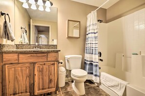 A bathroom with a wooden vanity, a toilet, a shower with a blue and white striped curtain, and a mirror above the vanity.