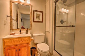A bathroom with a wooden vanity, a white toilet, a glass-enclosed shower, and a framed picture on the wall.