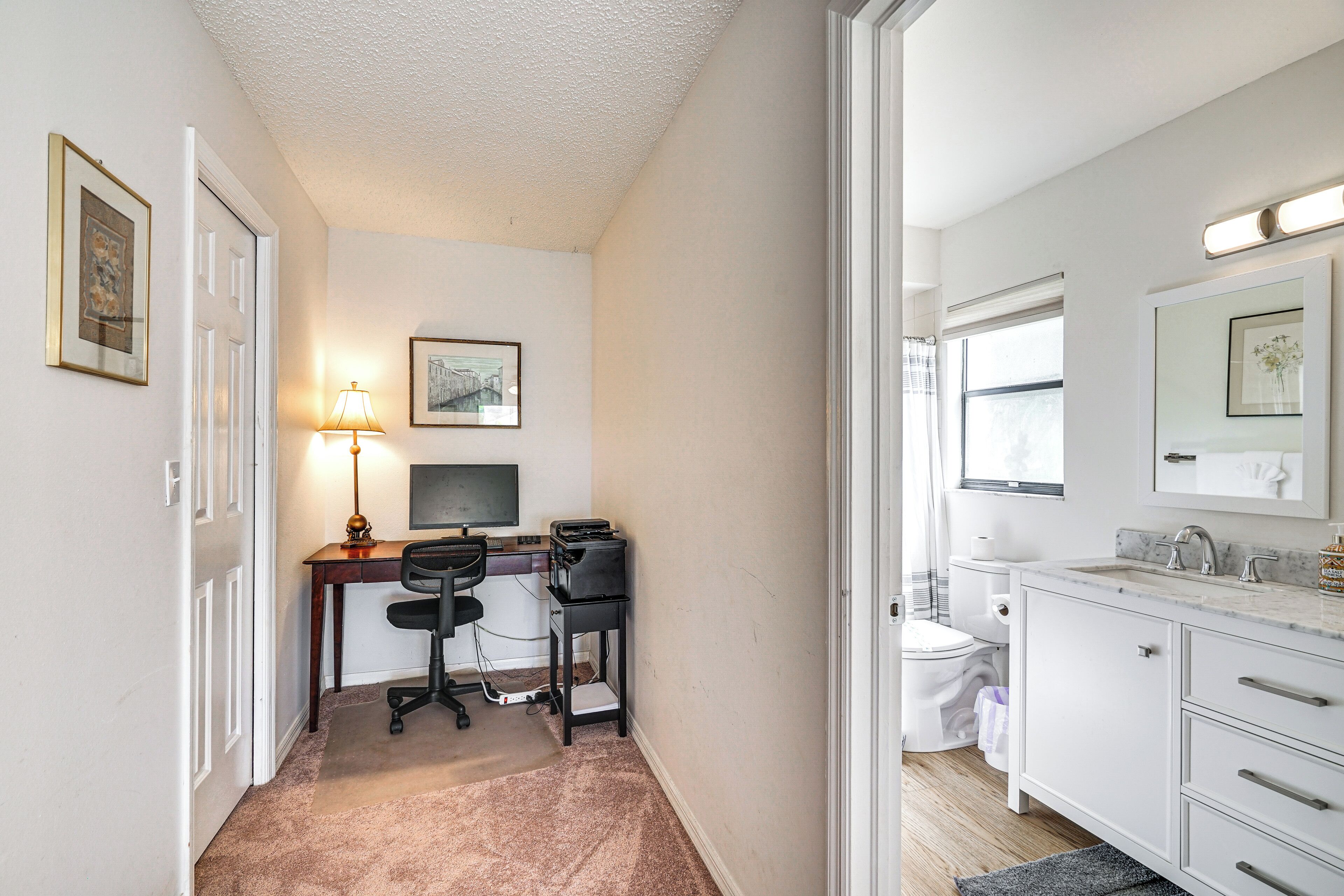 A compact bedroom with a desk, a chair, a bed, and a bathroom with a sink and toilet.
