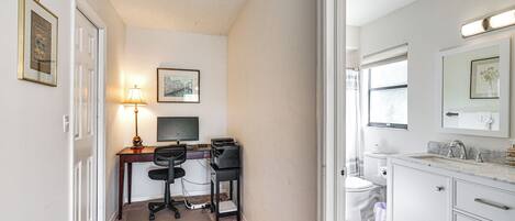 A compact bedroom with a desk, a chair, a bed, and a bathroom with a sink and toilet.