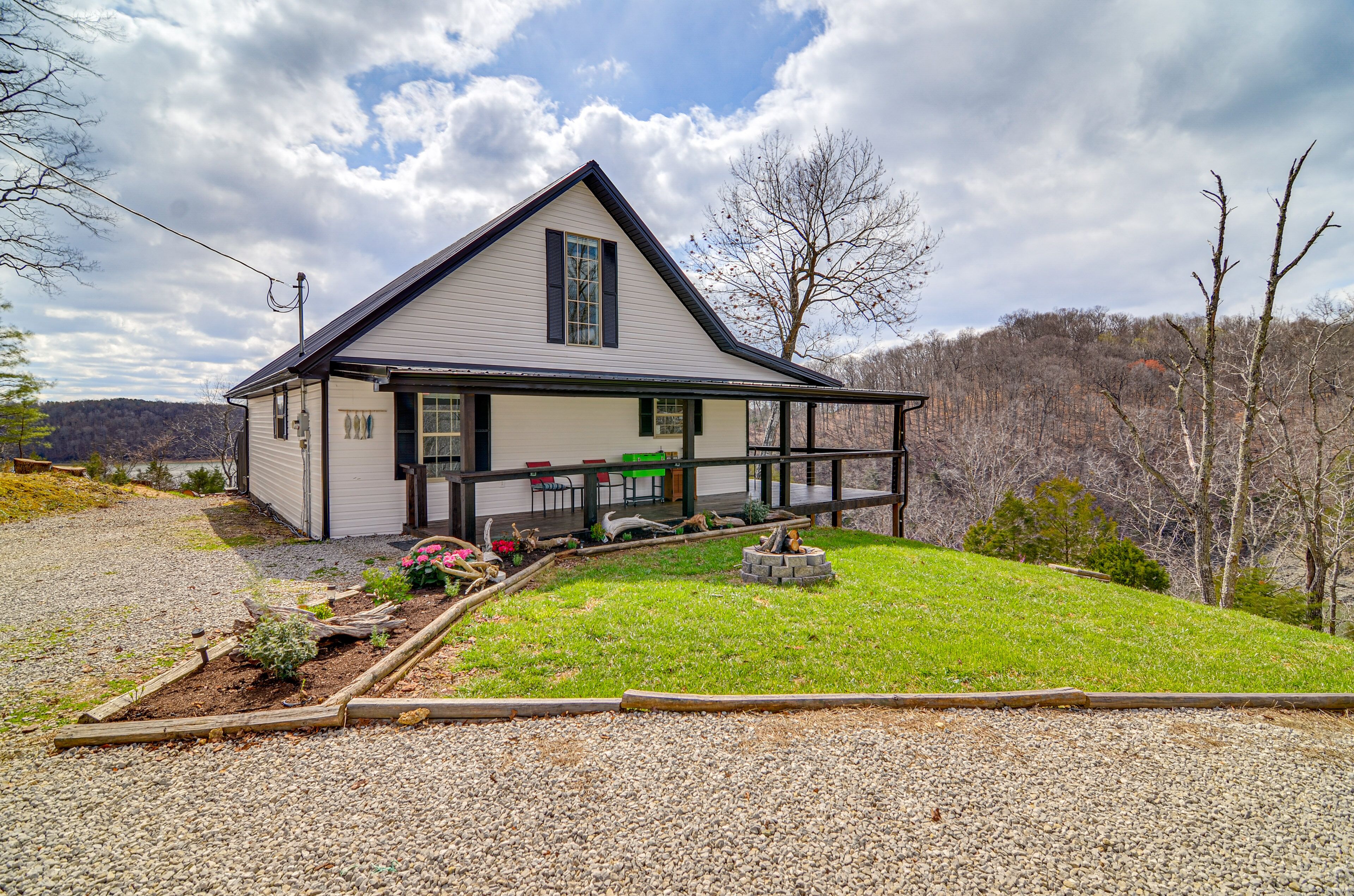 A two-story house with a covered porch, a small garden, and a view of a forested hill.