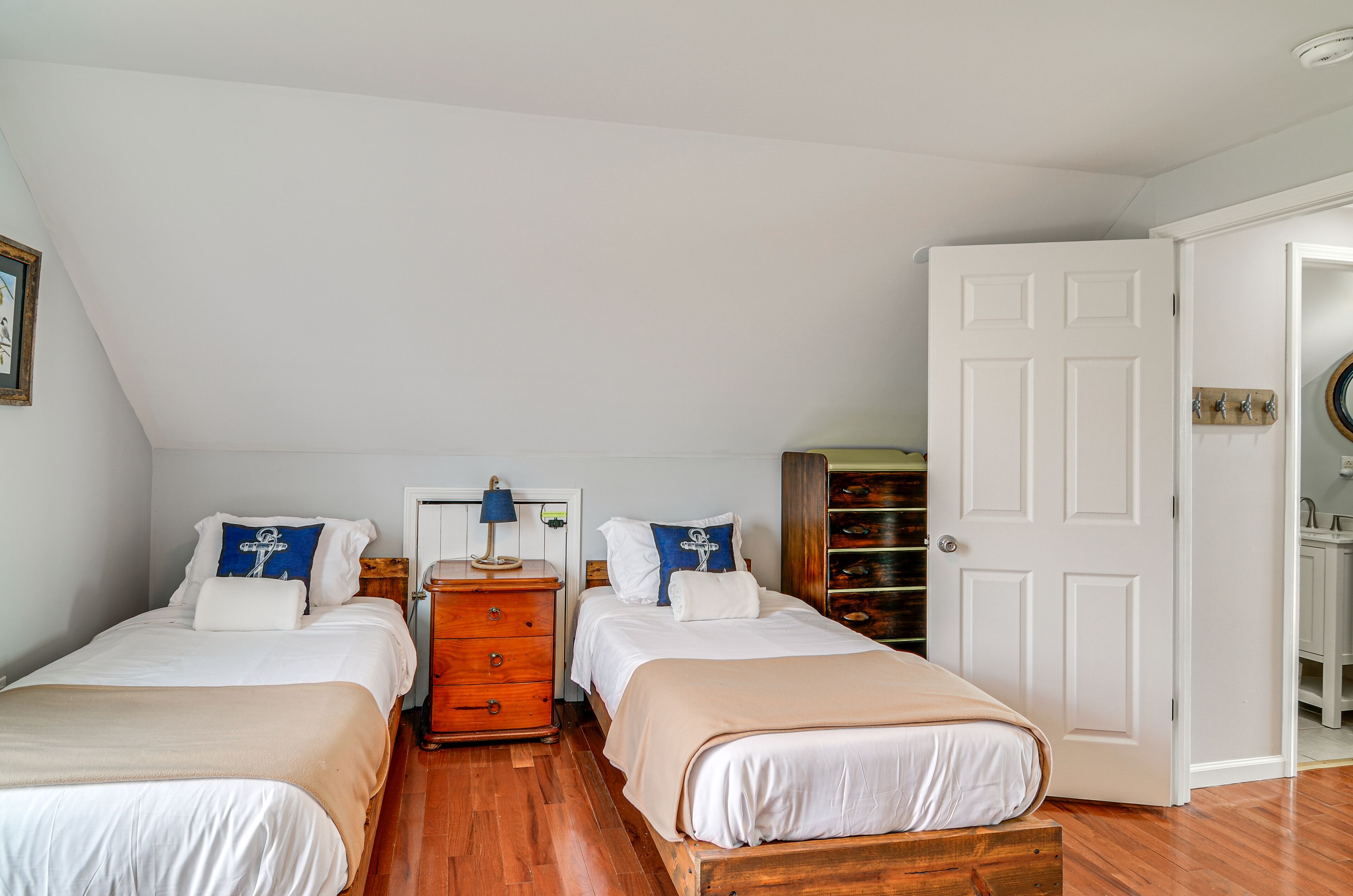 A bedroom with two single beds, a wooden dresser, a white door, and a small wooden shelf.