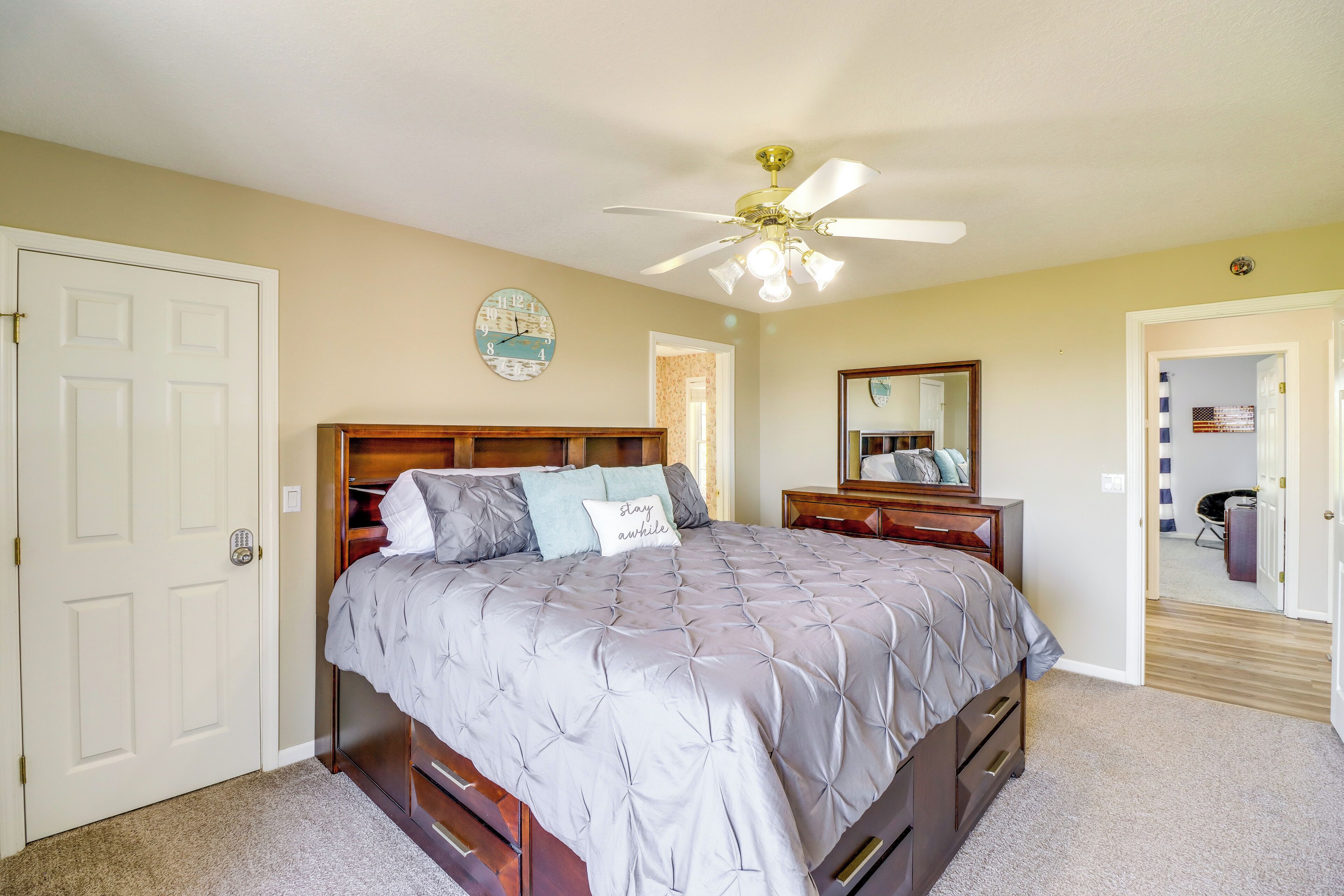 A bedroom with a bed, a ceiling fan, a clock, and a door.
