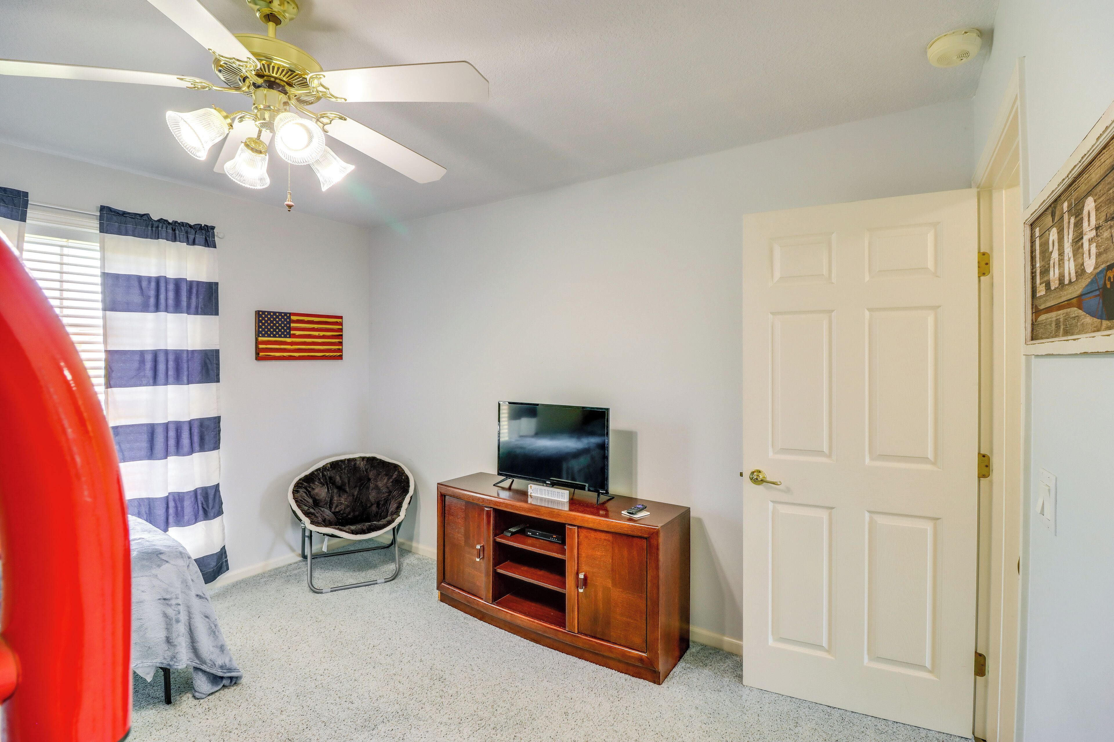 A room with a wooden entertainment center, a ceiling fan, a flag, and a door.