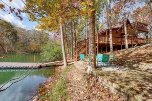 A cabin with a deck overlooking a lake, surrounded by trees and a wooden dock. - Hocking Hills Lake Gem w/ Hot Tub, Dock, 100 Acres (Hamden)