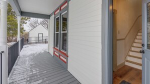 A covered porch with a wooden floor, a white exterior wall, and a glass door leading to a staircase. - Charming Stevensville Home w/ Open Yard! (Stevensville)
