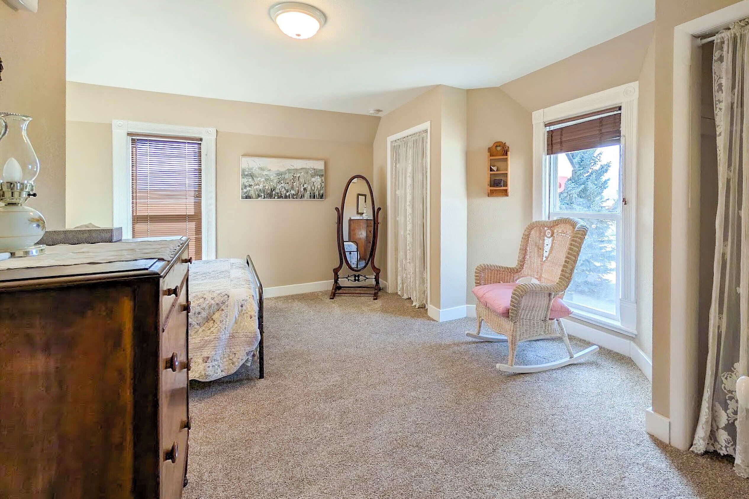 A cozy room with a wooden dresser, a rocking chair, a mirror, and a window with curtains.