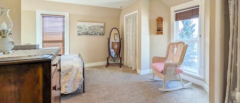 A cozy room with a wooden dresser, a rocking chair, a mirror, and a window with curtains.