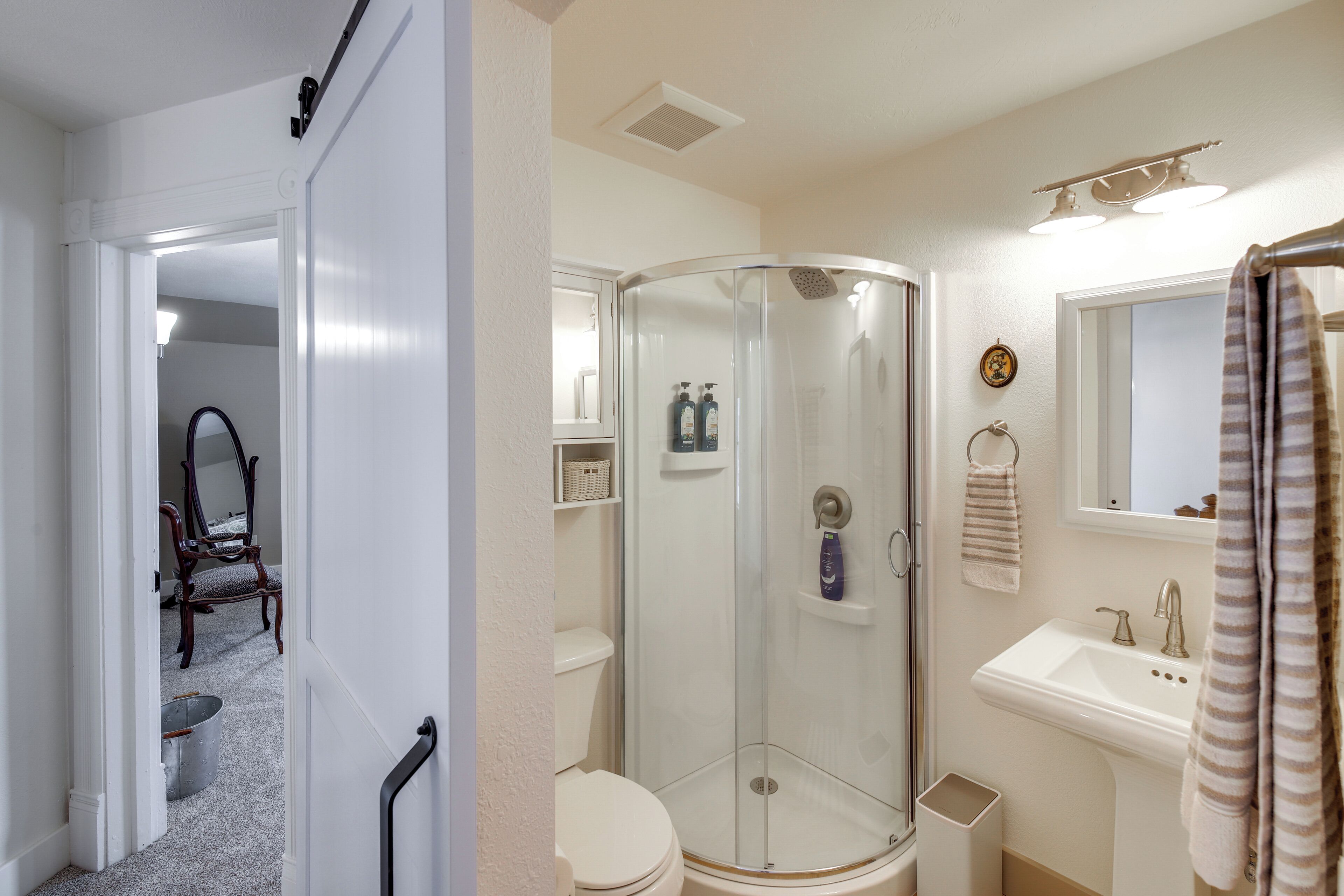 A bathroom with a glass shower enclosure, a toilet, a sink, and a mirror.