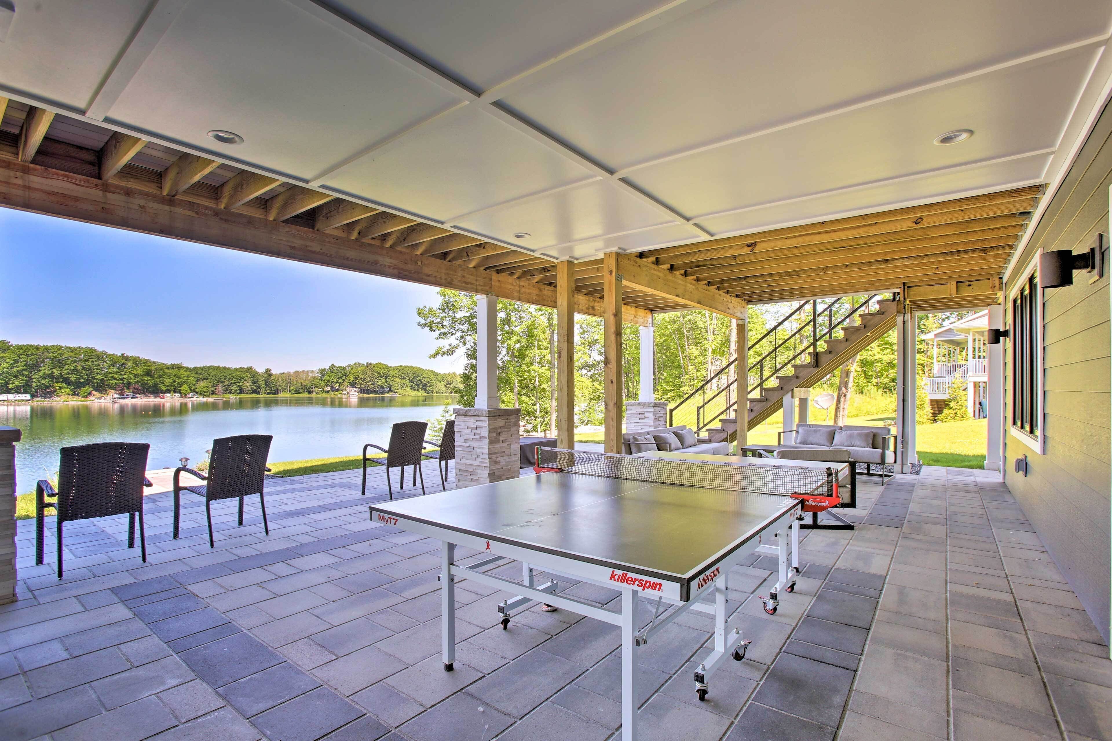An outdoor patio with a ping pong table, chairs, and a view of a lake.