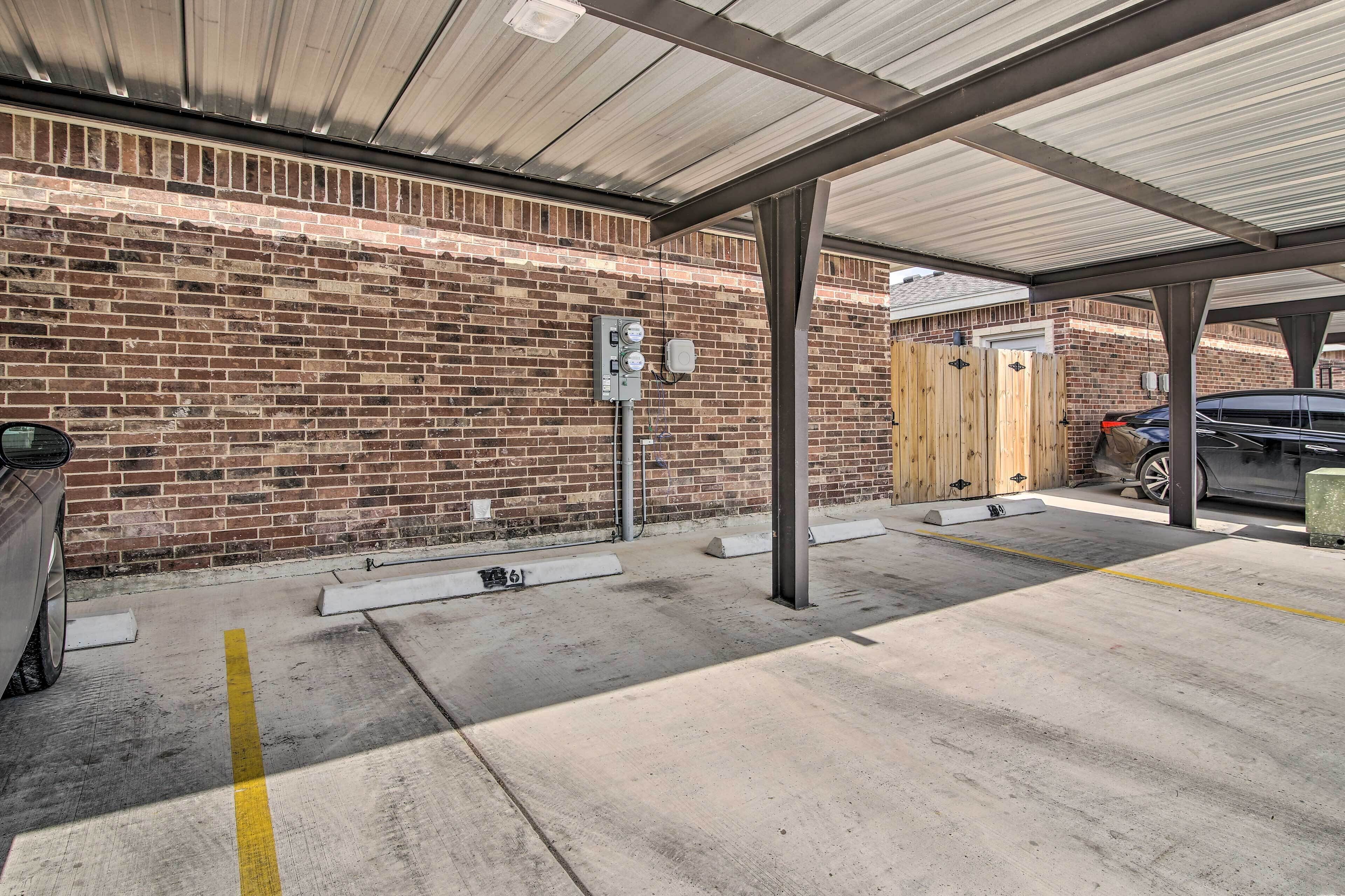 A covered parking area with a brick wall, a concrete floor, and a wooden fence.