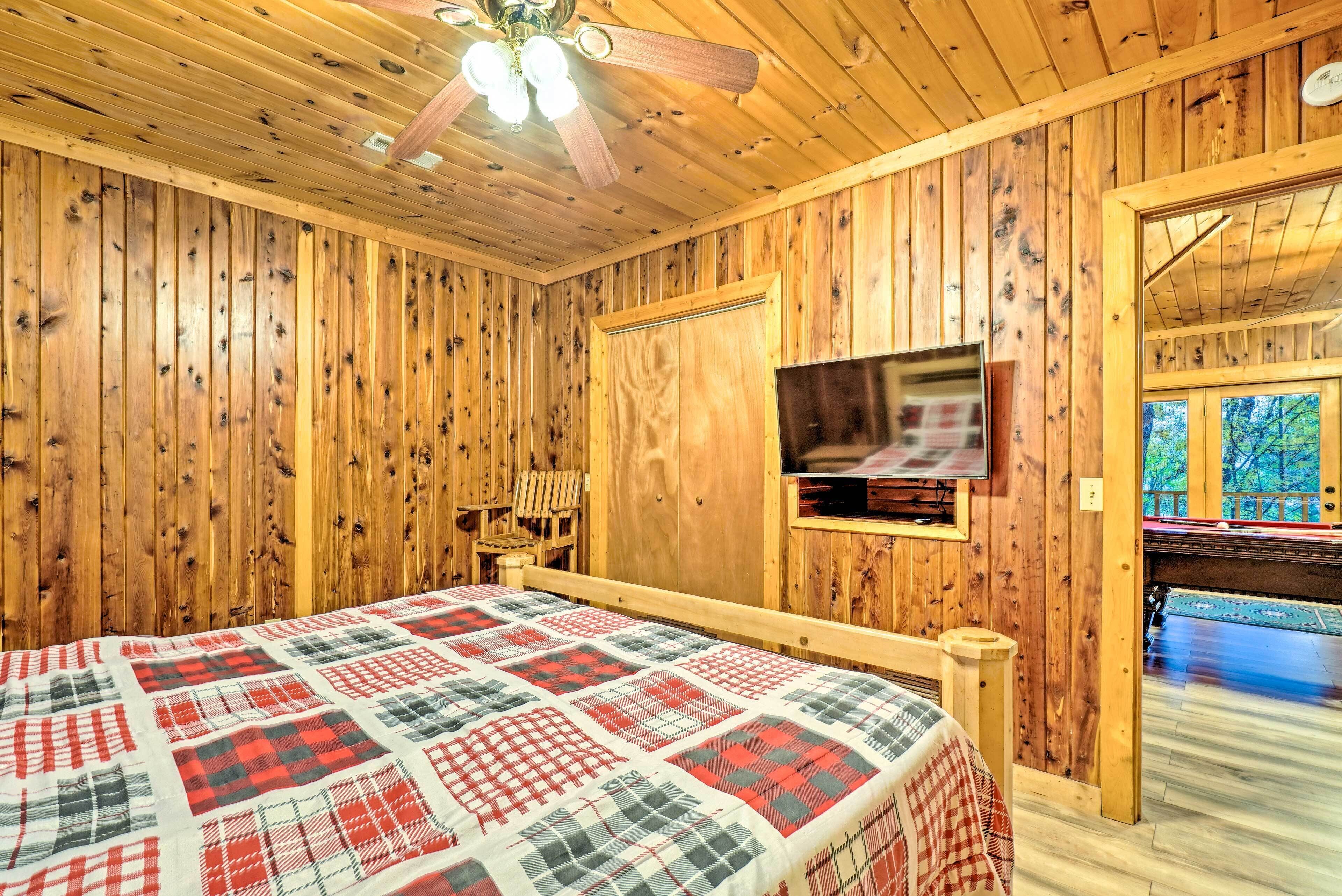 Una habitación con paneles de madera, una cama, un ventilador de techo, un televisor y vistas a una terraza exterior.
