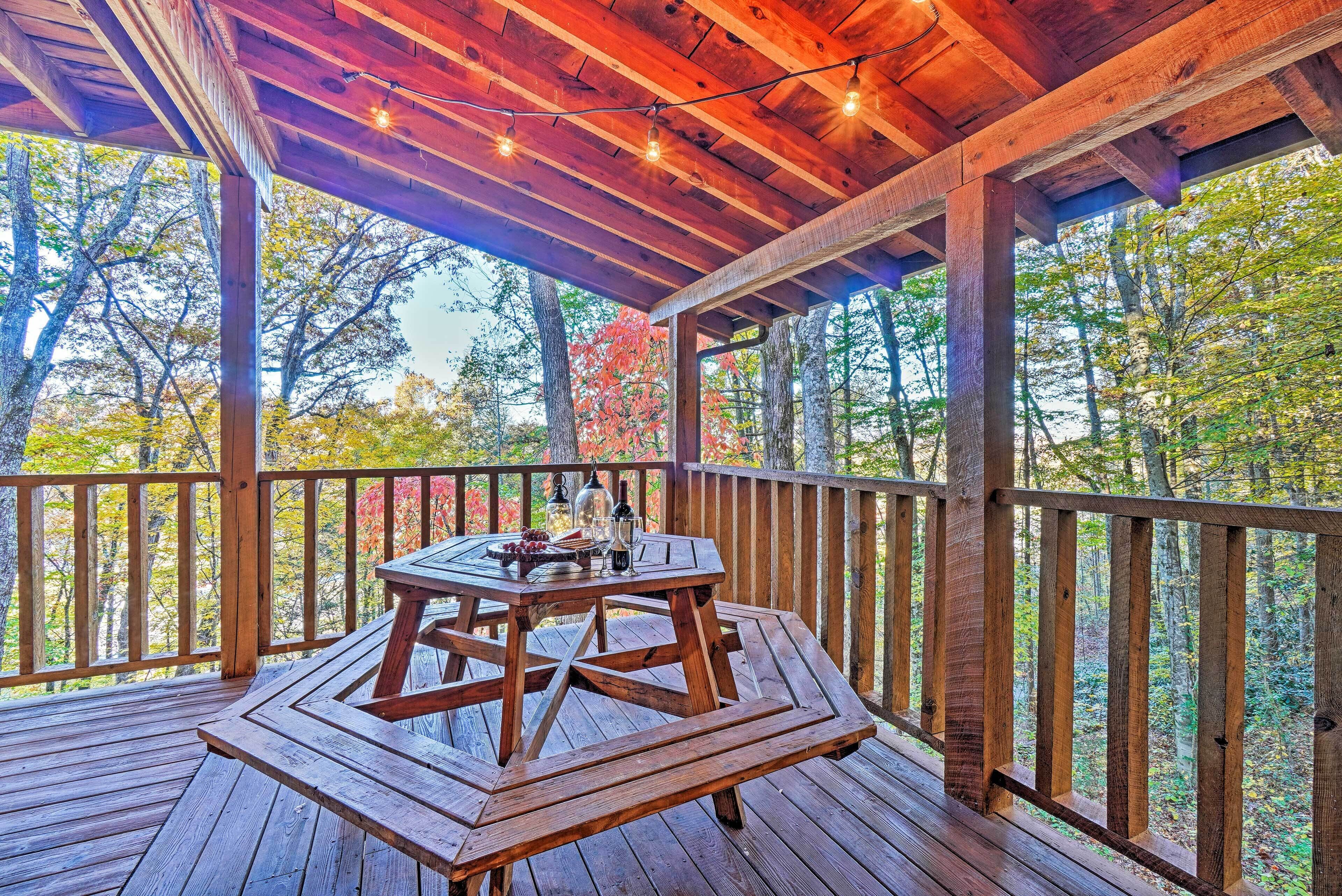 A wooden deck with a table and chairs, surrounded by a wooden railing, overlooking a forested area.