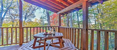 A wooden deck with a table and chairs, surrounded by a wooden railing, overlooking a forested area.