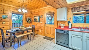 Ein Interieur einer Holzhütte mit einem Esstisch, Bänken, einer Küche mit roter Arbeitsplatte und einem großen Fenster.