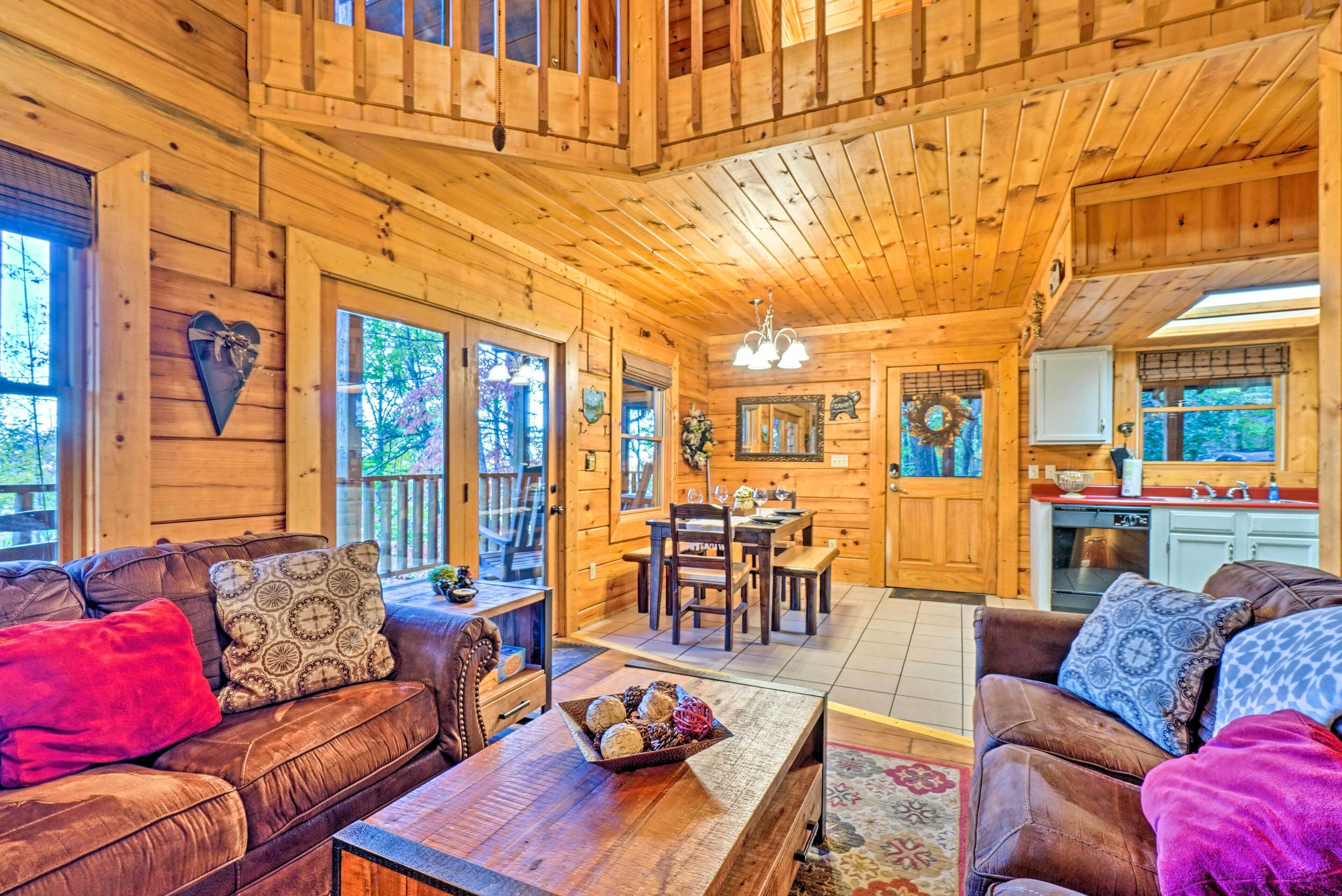 Interior acogedor de una cabaña con paredes y techos de madera, un comedor con candelabro y una cocina con lavaplatos y armarios.
