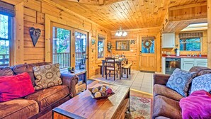 Ein gemütliches Blockhaus-Interieur mit Holzwänden und -decken, einem Essbereich mit einer Pendelleuchte und einer Küche mit Spüle und Schränken.