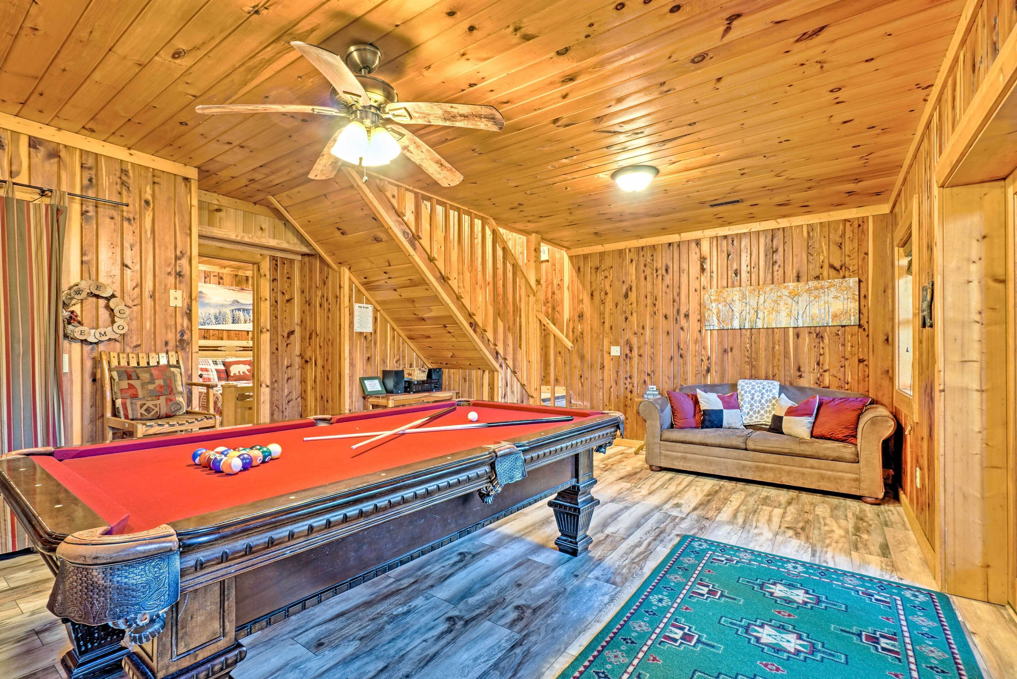 A wooden interior with a pool table, a sofa, and a staircase.