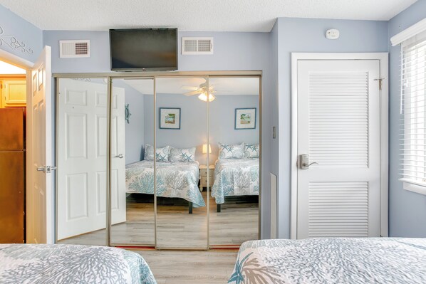 A bedroom with a sliding door closet, a bed with a patterned bedspread, a ceiling fan, and a mounted TV.