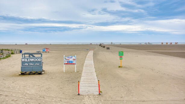 Een strand met een houten looppad dat leidt naar een bord waarop staat 