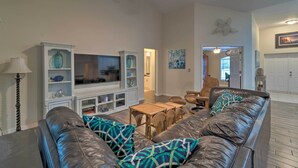 A living room with a leather sofa, a TV, and a dining area with wicker furniture.