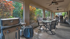 A covered patio area with a Weber Spirit grill, outdoor seating, and large windows offering views of trees.