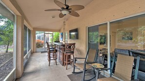 A covered patio area with a ceiling fan, wooden chairs, a bar area, and large sliding glass doors.