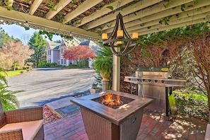 A covered outdoor patio with a fire pit, grilling station, and wicker furniture.