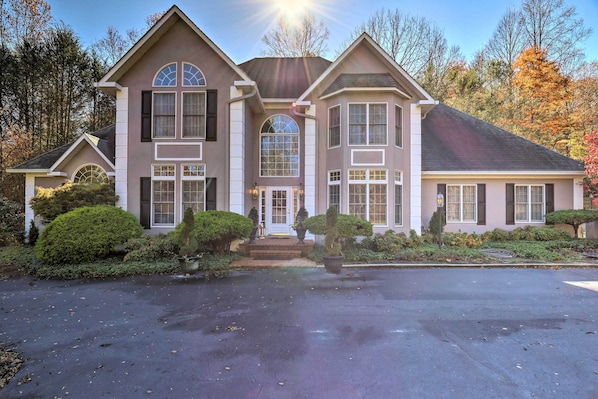 A large, two-story house with a symmetrical facade, a central entrance with a small porch, and a driveway leading to the front door.