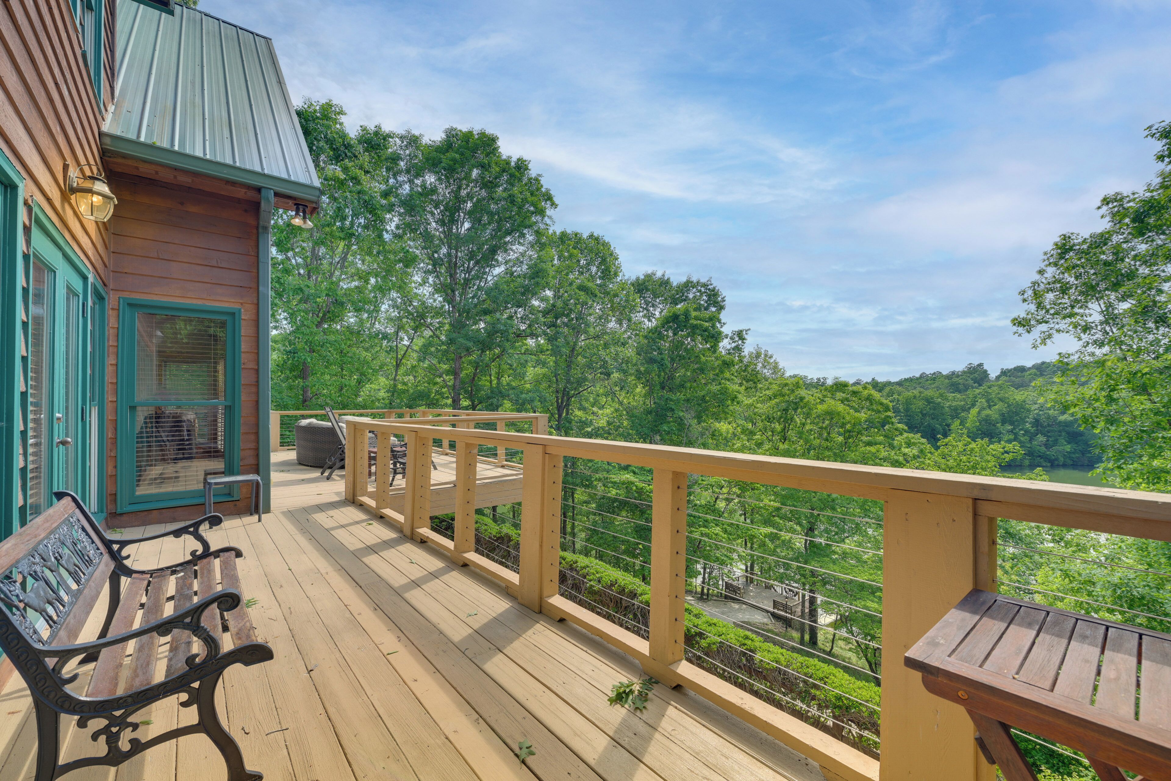 A wooden deck with a bench, a small building with a green door, and a view of a forested area.
