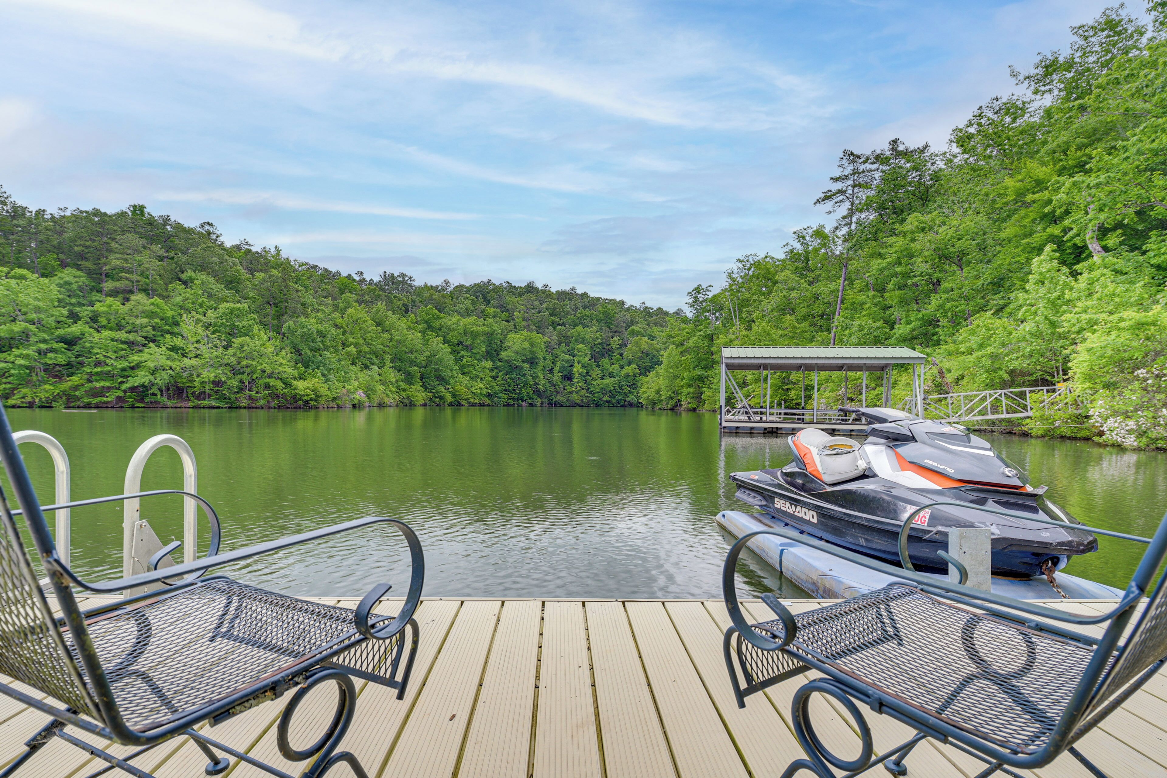 A wooden dock with metal chairs and a jet ski docked on the right.