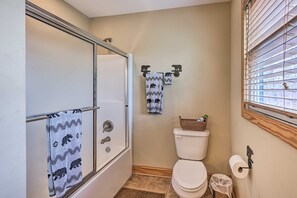 A bathroom with a glass-enclosed shower, a toilet, and a window with blinds.