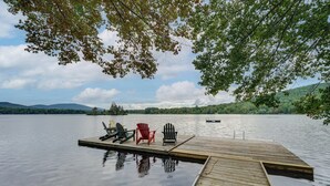 A wooden dock extending into a calm lake with three Adirondack chairs and a red chair. - Lakefront Paradise Near Okemo & Killington (Mount Holly)