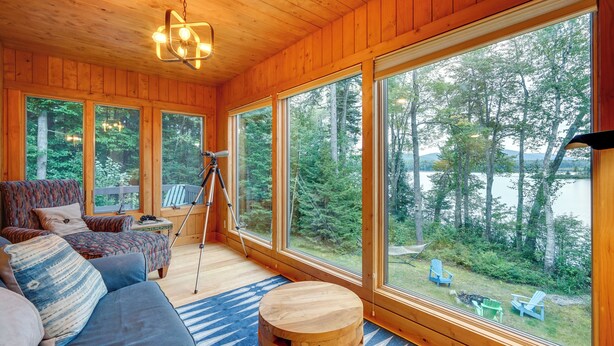 A cabin with large windows, a sofa, a tripod, and outdoor seating. - Lakefront Paradise Near Okemo & Killington (Mount Holly)