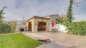 Un patio trasero con zona de barbacoa, mobiliario exterior e iluminación con luces colgantes.