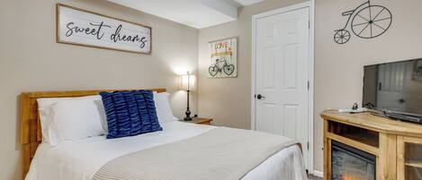 A neatly arranged bedroom with a bed, a television on a wooden stand, a fireplace, and wall decorations including a bicycle and a sign that says "sweet dreams".