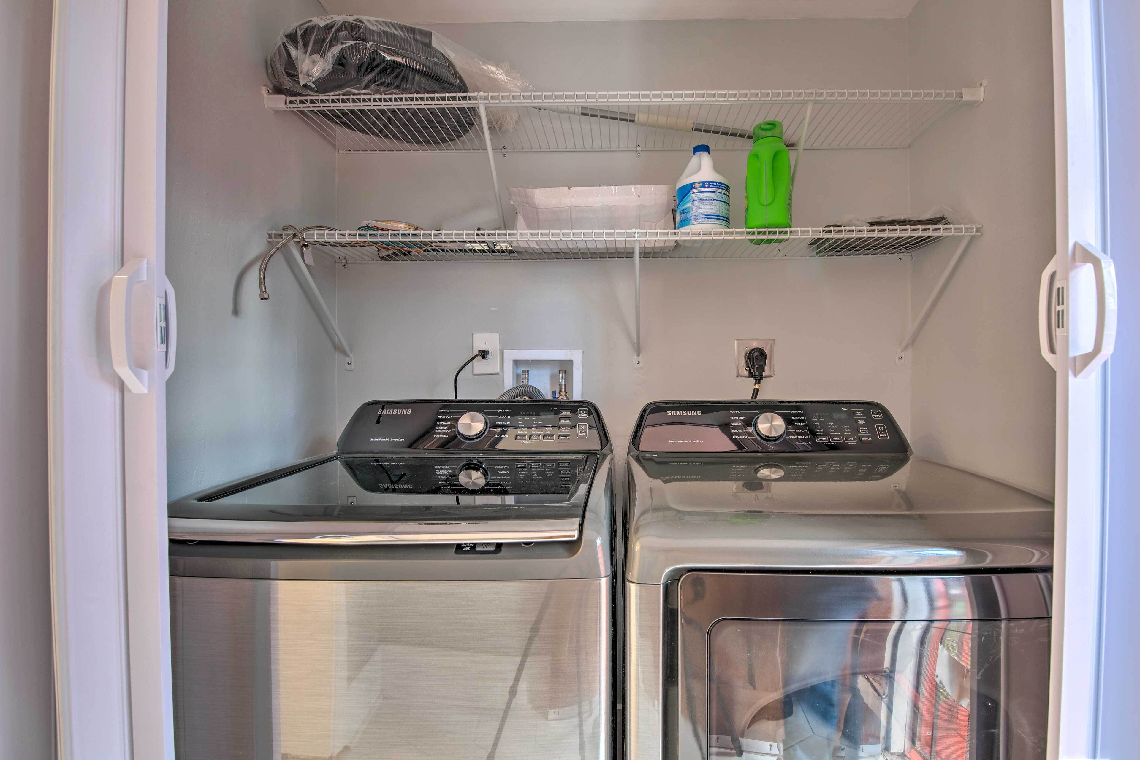 A laundry room with two washing machines, a shelf with cleaning supplies, and a power outlet.
