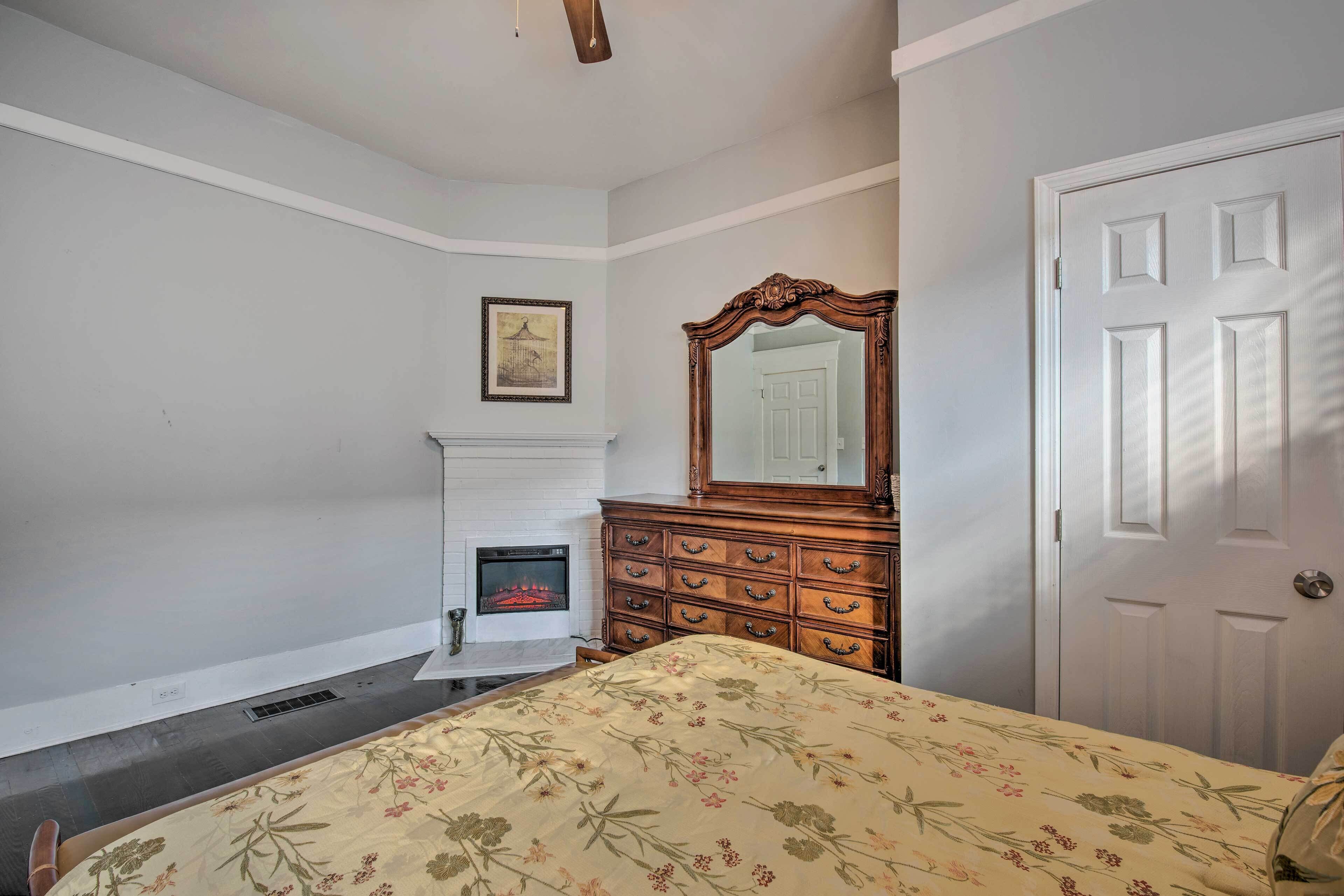 A bedroom with a bed, a dresser, a mirror, a fireplace, and a door.