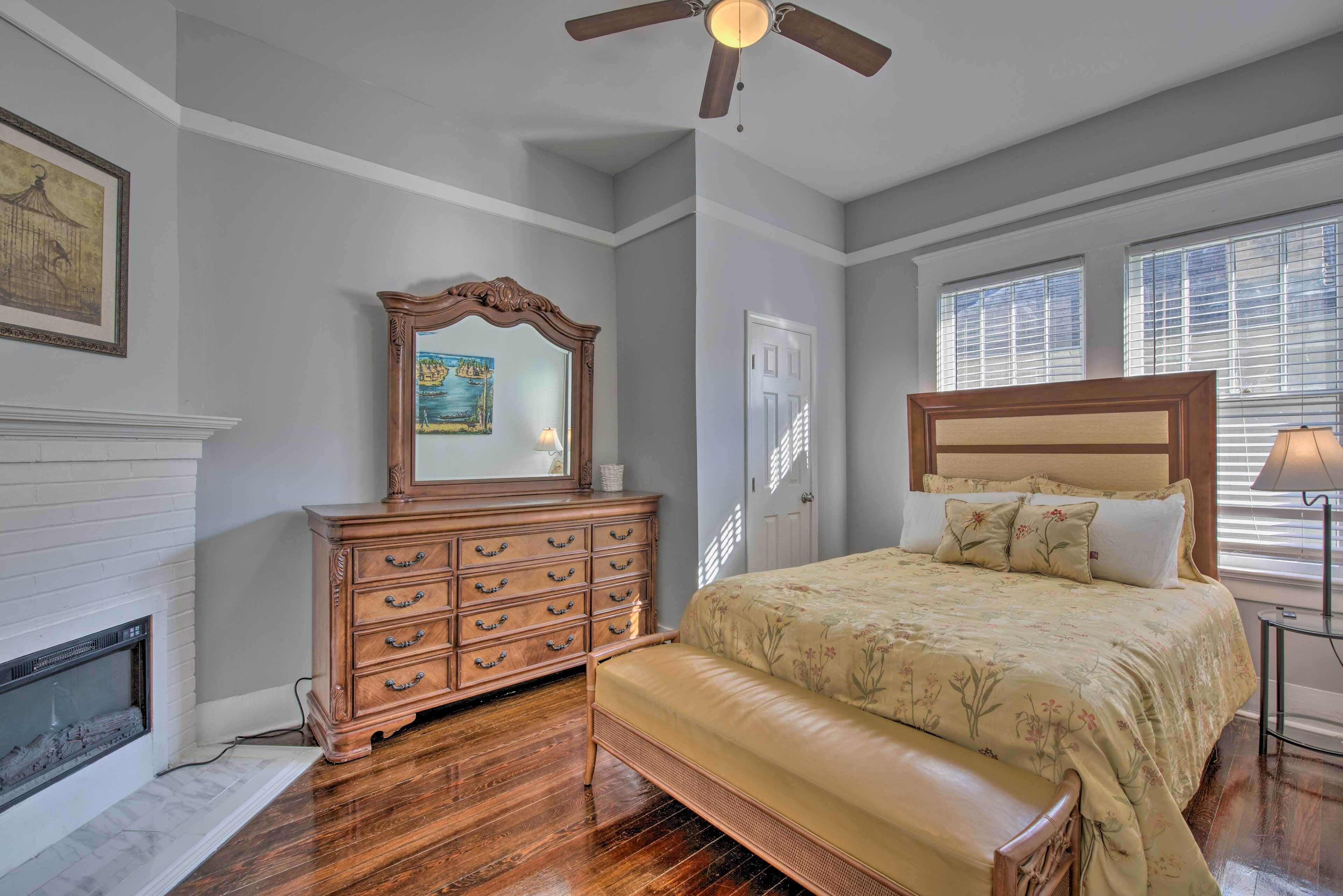 A bedroom with a wooden bed, a dresser, a mirror, a fireplace, and a ceiling fan.