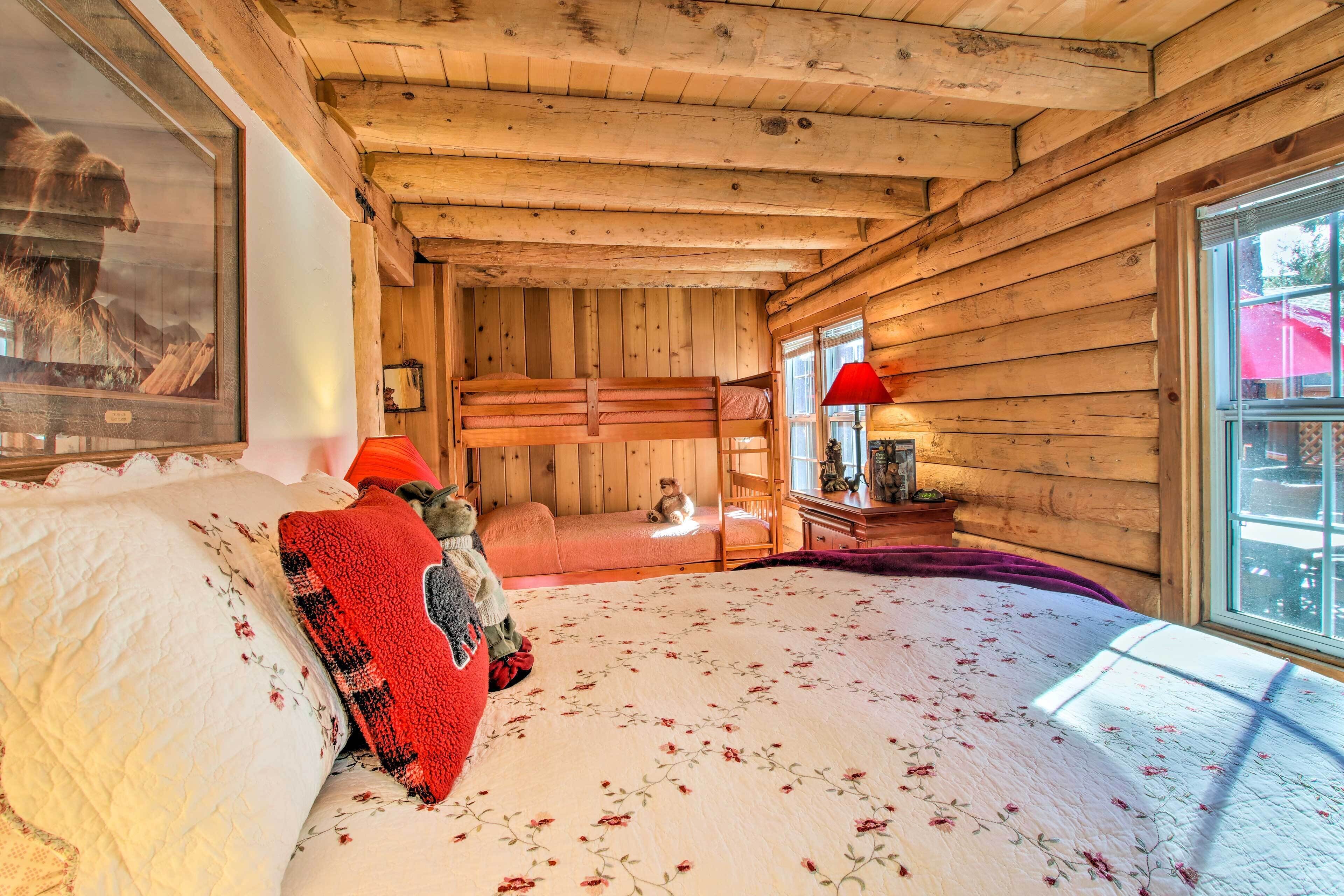A cozy cabin-style room with a wooden ceiling, a bunk bed, a large window with a view, and a framed picture on the wall.
